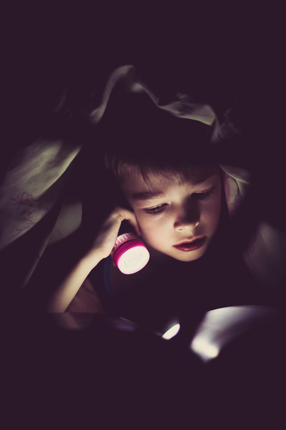 Ein Junge liest mit Taschenlampe unter der Bettdecke